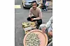 Abdelrahman and Ibrahim sit in front of their stall, selling feseekh, ringa and mussels. Abdelrahman is wearing a jumper with a traditional pattern, holding a smart phone, and smiling into the camera.