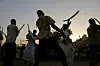 Men wearing white jalaib are dancing and wielding swords in a traditional wedding performance.