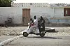 A family of five, a mother, a father, and three children, is driving on a white scooter in a street in Port Sudan.