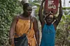 A still from Mambar Pierrette of a woman walking with a young girl who is carrying a pail on her shoulders.