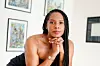 Ayofemi Kirby poses with her head propped up on her elbows behind a white background decorated with artworks.