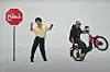 Draganov is dancing next to a red sign with Arabic writing, wearing black trousers, a yellow shirt, and a brown wig. Next to him, he is sitting on a red e-bike, wearing all black, sunglasses, and no wig.