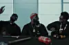 A screenshot of Stormzy, Odumodublvck, and Zlatan in the music video for Odumodu’s “Pay Me.” All three artists are wearing all-black outfits and are seated in front of a table with power tools on it.