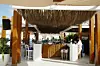 The bar of a beach restaurant, made of wood, bamboo straws, and white textiles. The blue Mediterranean is in the background.