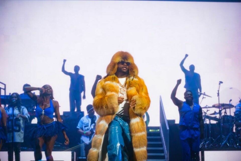 Davido live on stage wearing a fur coat, sunglasses, white t-shirt, blue jeans and a chunky silver c
