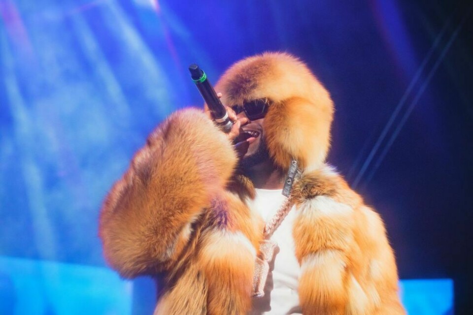 Davido live on stage wearing a fur coat, sunglasses, white t-shirt, blue jeans and a chunky silver chain