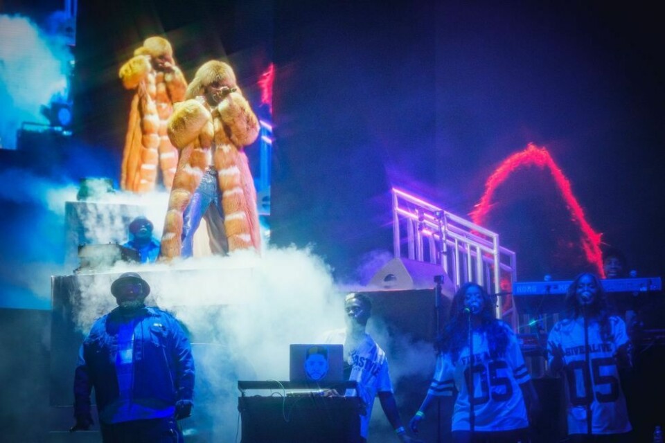 Davido live on stage wearing a fur coat, sunglasses, white t-shirt, blue jeans and a chunky silver chain