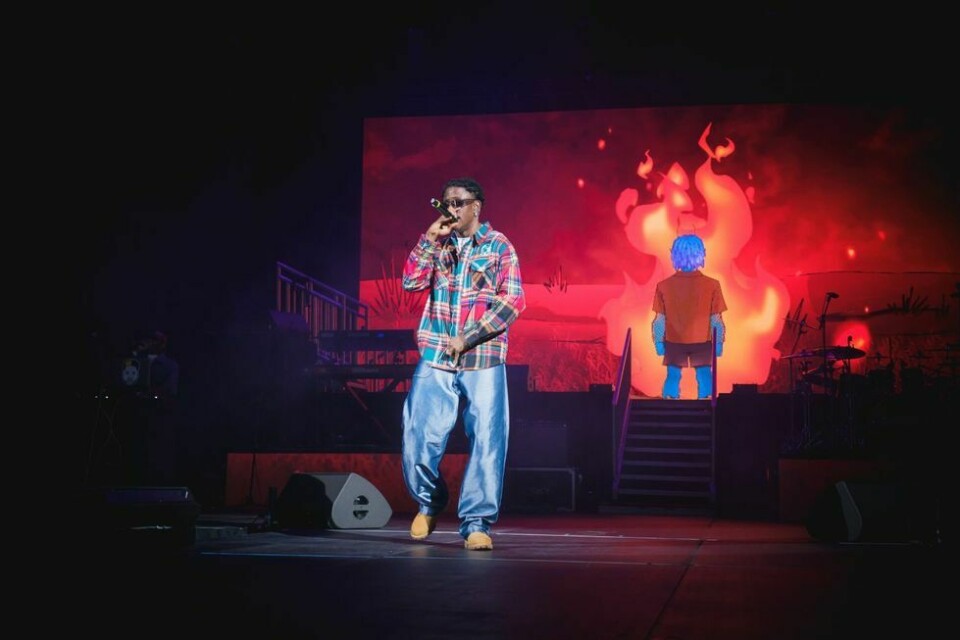 Victony performing live on stage with a mic. He wears a checkered shirt and blue jeans.