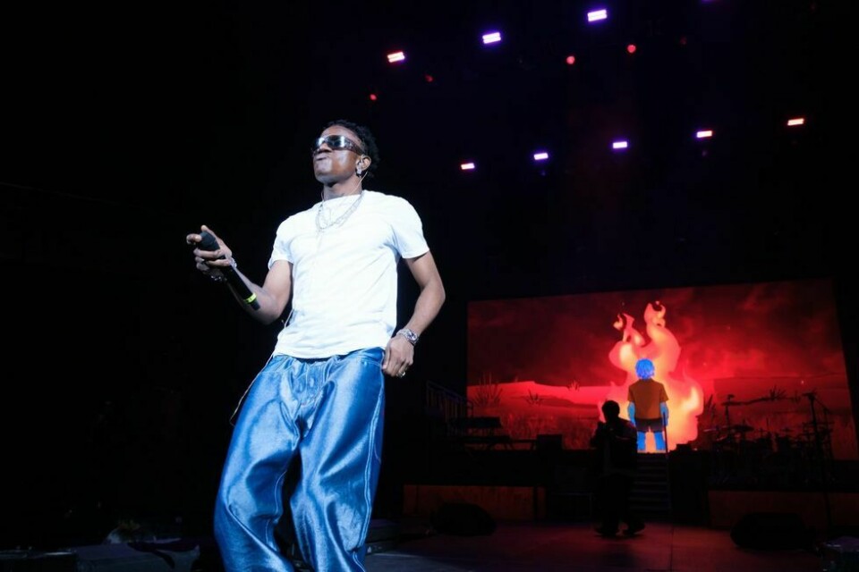 Victony performing live on stage with a mic. He wears a white t-shirt and blue jeans.